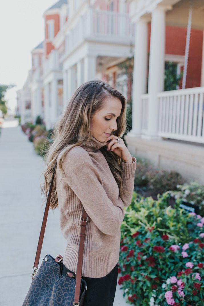 Woman wearing tan sweater in autumn while standing near bushes