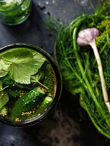Open jar of homemade pickles near garden vegetables