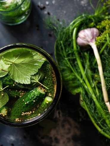 Open jar of homemade pickles near garden vegetables