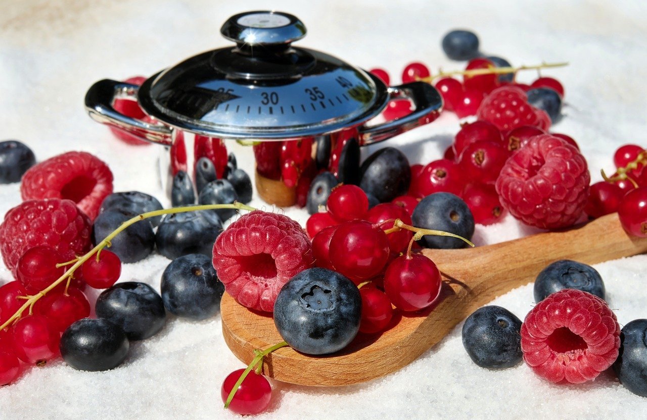 Wooden spoon full of berries for making jam near small cooking device