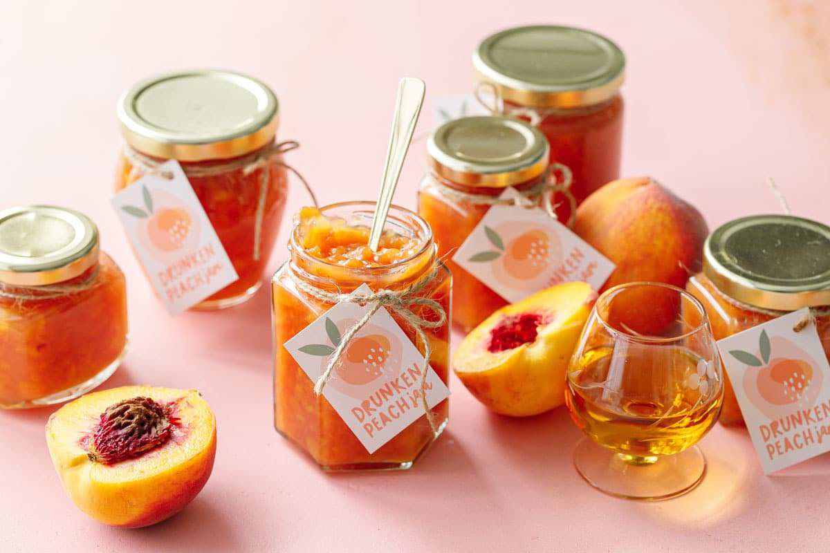 Jars of drunken peach jam with utensil sticking out of one