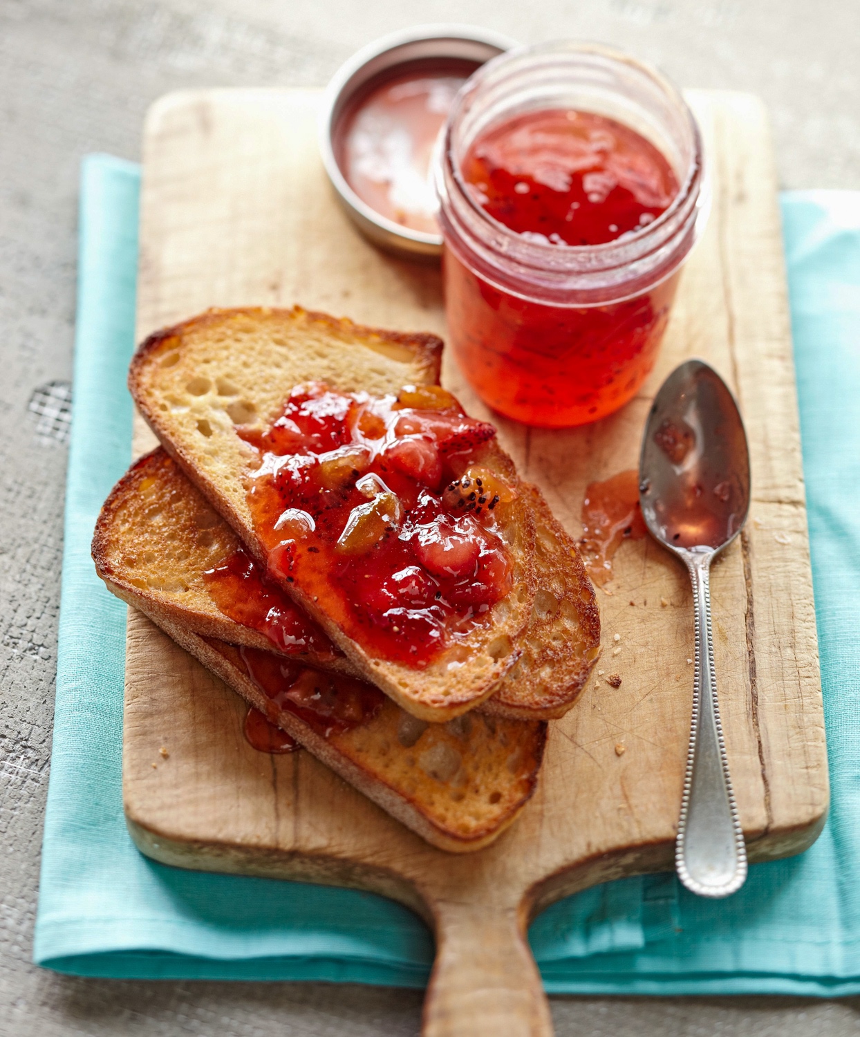 Open jar of strawberry-kiwi jam near toast on cutting board