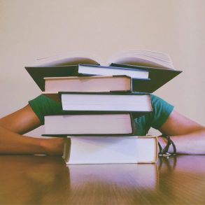 Frustrated student with head on desk behind stack of books to symbolize debt