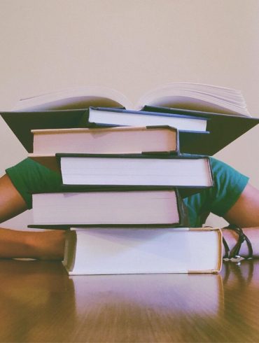 Frustrated student with head on desk behind stack of books to symbolize debt
